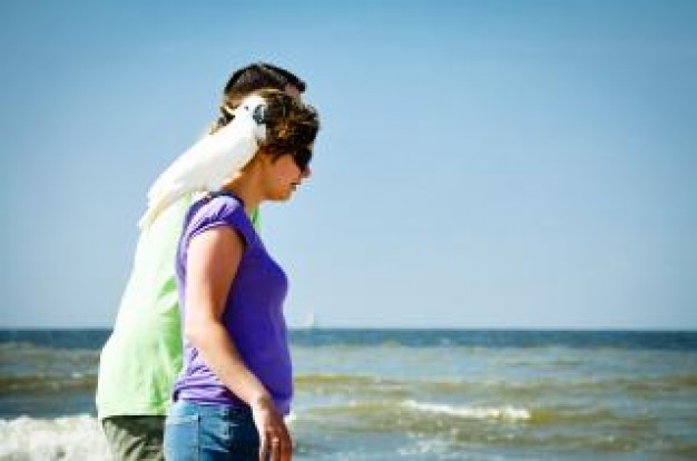 woman walking with parrot on shoulder with sea background